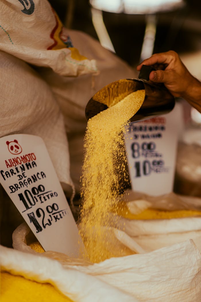 why-choose-us Close-up of hand pouring Bragança flour from scoop in a market with price tags visible.